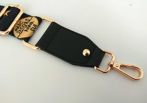 Macro d'une bandoulière noire tressée avec mousquetons dorés et détails en cuir