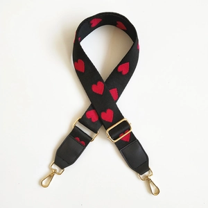 Close-up of adjustable bag strap with red heart embroidery and gold metal buckles