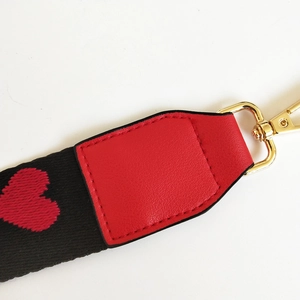 Close-up of ethnic style nylon bag strap with red heart patterns and gold metal buckles