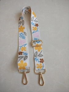 Close-up of floral canvas bag strap with golden metal buckles and adjustable slider