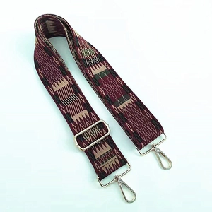 Detail of adjustable bag strap featuring burgundy jacquard geometric patterns and gold clips