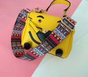 Détail du sac bandoulière jaune avec visage souriant et large sangle tissée style ethnique