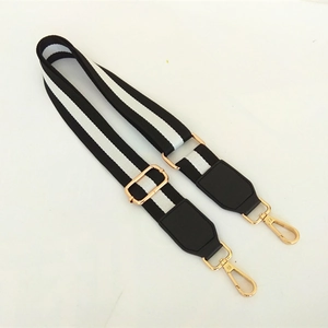 Detail of adjustable black and white striped shoulder strap with gold metal buckles