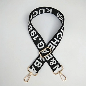 Close-up of wide adjustable woven bag strap with letter patterns and gold metal hooks