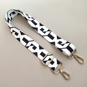 Detail of adjustable black and white geometric pattern bag strap with gold metal hardware