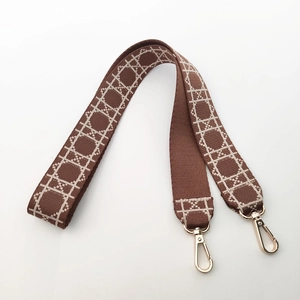 Detail of wide brown woven bag strap with white geometric jacquard and gold metal clips