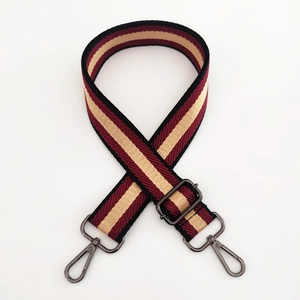 Détail d'une bandoulière en toile rayée rouge, beige et noire avec crochets foncés