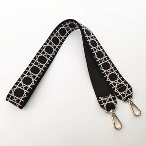 Detail of wide woven strap featuring black and white geometric patterns with gold lobster clasps