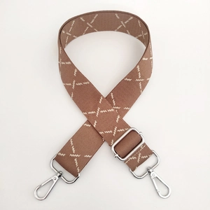 Detail of adjustable brown woven bag strap with white geometric stitching and silver hooks