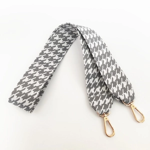 Detailed view of grey houndstooth thick wide bag strap with golden lobster clasps