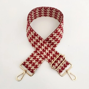 Detail eines rot-weißen Hahnentritt-Taschenriemens mit goldenen Metallkarabinern