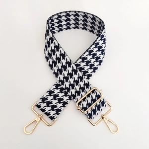 Detail eines verstellbaren schwarz-weißen Hahnentritt-Taschenriemens mit Gold-Schnallen