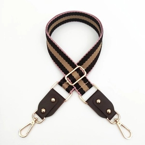 Close-up of tricolor woven wide shoulder strap with golden lobster clasps and rivets