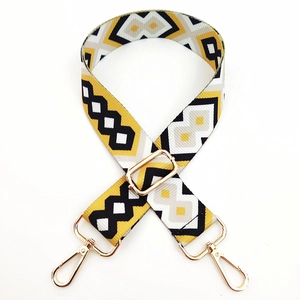 Detail of adjustable geometric woven bag strap with yellow patterns and gold metal hooks