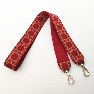 Macro detail of red woven shoulder strap with gold metal hooks and geometric pattern