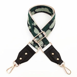 Detail of adjustable woven canvas bag strap with green geometric patterns and gold clips