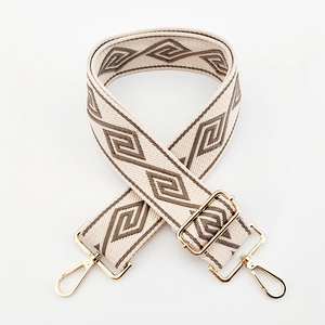 Close-up of wide canvas bag strap with beige and brown geometric patterns and gold buckles
