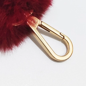 Macro shot of fluffy wine red faux fur ball bag charm with golden lobster clasp detail