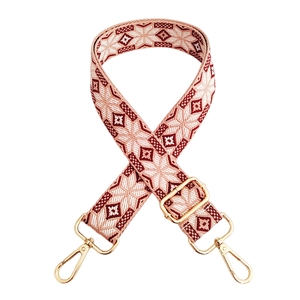 Detail of red and cream geometric embroidery on a wide crossbody strap with gold hardware