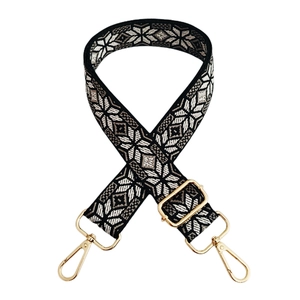 Detail of wide jacquard bag strap with geometric patterns and gold metal buckles