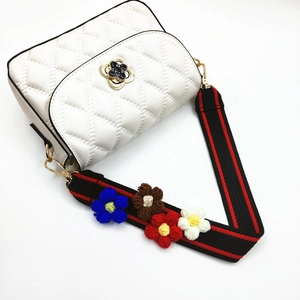 Detail of white quilted crossbody bag with handmade crochet flowers on a wide strap