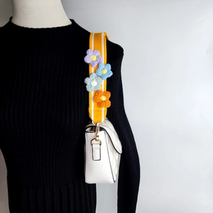 Detail of yellow woven bag strap with colorful crochet flowers and gold metal clips