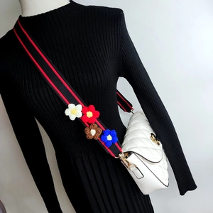 Detail of white quilted crossbody bag with red-black striped floral wide strap