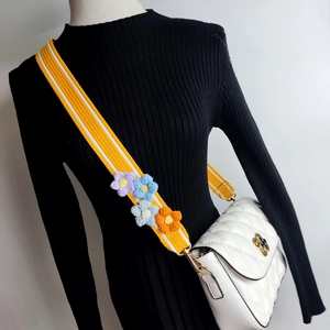 Detail of white quilted handbag featuring colorful 3D crochet flowers on yellow wide strap