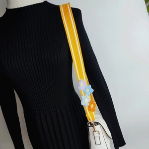 Close-up of a yellow knitted bag strap with colorful crochet flowers and golden hooks