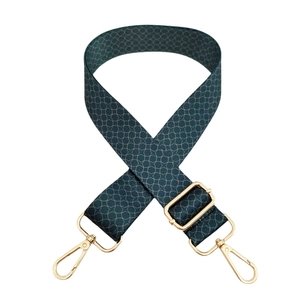 Close-up of wide green adjustable bag strap with geometric pattern and gold metal hooks