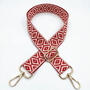 Detail of red and cream geometric jacquard woven bag strap with gold metal lobster clasps