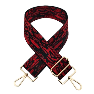 Detail of wide red and black abstract pattern bag strap with gold metal hardware
