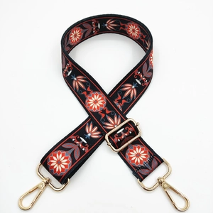 Close-up of ethnic floral embroidery on a black wide bag strap with gold metal hooks