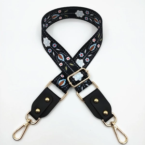 Detail of floral embroidered bag strap with golden rivets and adjustable metal buckles