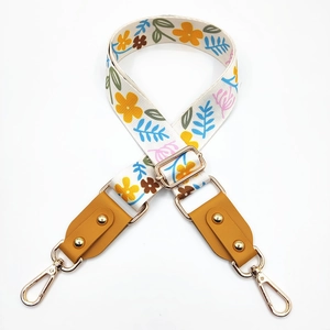 Detail view of floral print canvas bag strap with golden rivets and lobster clasps