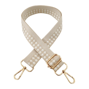 Close-up of beige geometric checkered woven strap with polished gold metal buckles