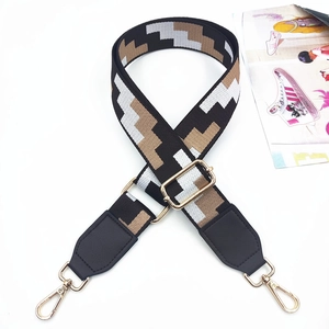 Detail of adjustable geometric patterned woven bag strap with golden metal swivel hooks