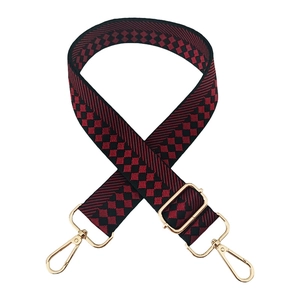 Detail of red and black checkered crossbody strap with golden lobster clasps and buckles
