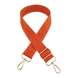 Detail of orange woven bag strap with diamond jacquard pattern and gold metal hooks