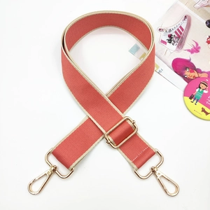 Close-up of wide woven canvas bag strap in coral red with gold lobster clasps and buckles