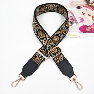 Detail of bohemian floral embroidery on wide woven bag strap with gold metal hooks