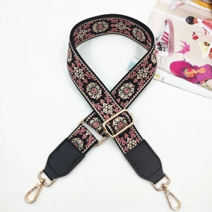Close-up of ethnic style floral embroidery on black bag strap with gold metal hooks