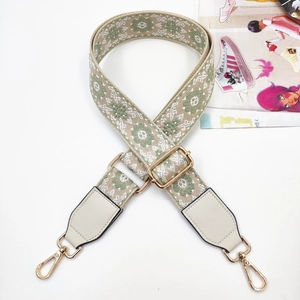 Detail of green floral woven bag strap with golden metal hooks and leather ends