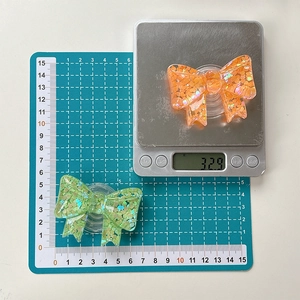 Macro detail showing bow glitter phone grip dimensions of 60mm width and weight of 32.9g