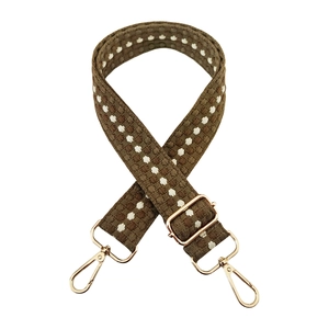 Detail of a thick woven strap with brown pattern and gold metal hardware clips