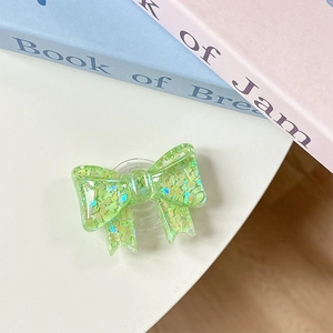 Close-up of a green glitter bow phone grip with heart sequins on a desk setup