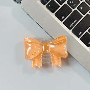Detail of an orange glitter bow phone grip with a retractable transparent socket base