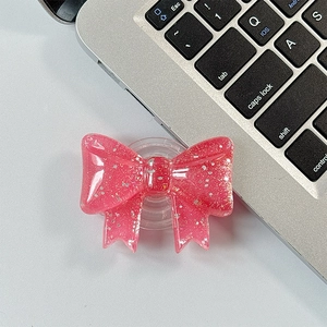 Detail of a pink glitter bow foldable phone grip stand on a gray office desk