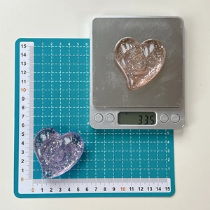 Macro shot of heart-shaped glitter phone grips showing 33.5g weight on a scale