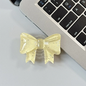 Close-up of a pale yellow resin glitter bow cell phone socket stand on a gray surface